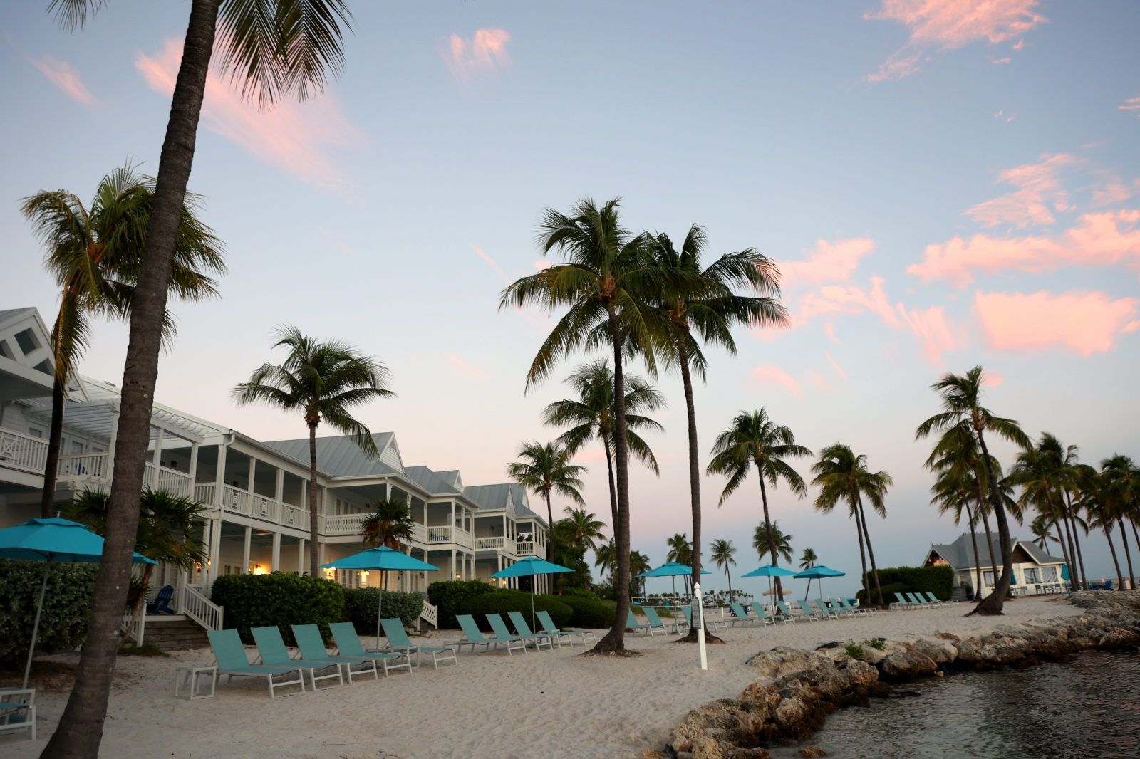 A beachfront hotel with multiple balconies, palm trees, and beach chairs.