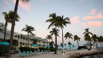 A beachfront hotel with multiple balconies, palm trees, and beach chairs.