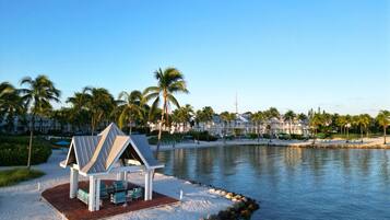 A beachside resort with a small pavilion, palm trees, and a calm lake.