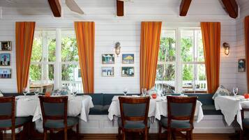 Dining area at Butterfly Cafe with orange curtains, white table settings, and a window-side bench.