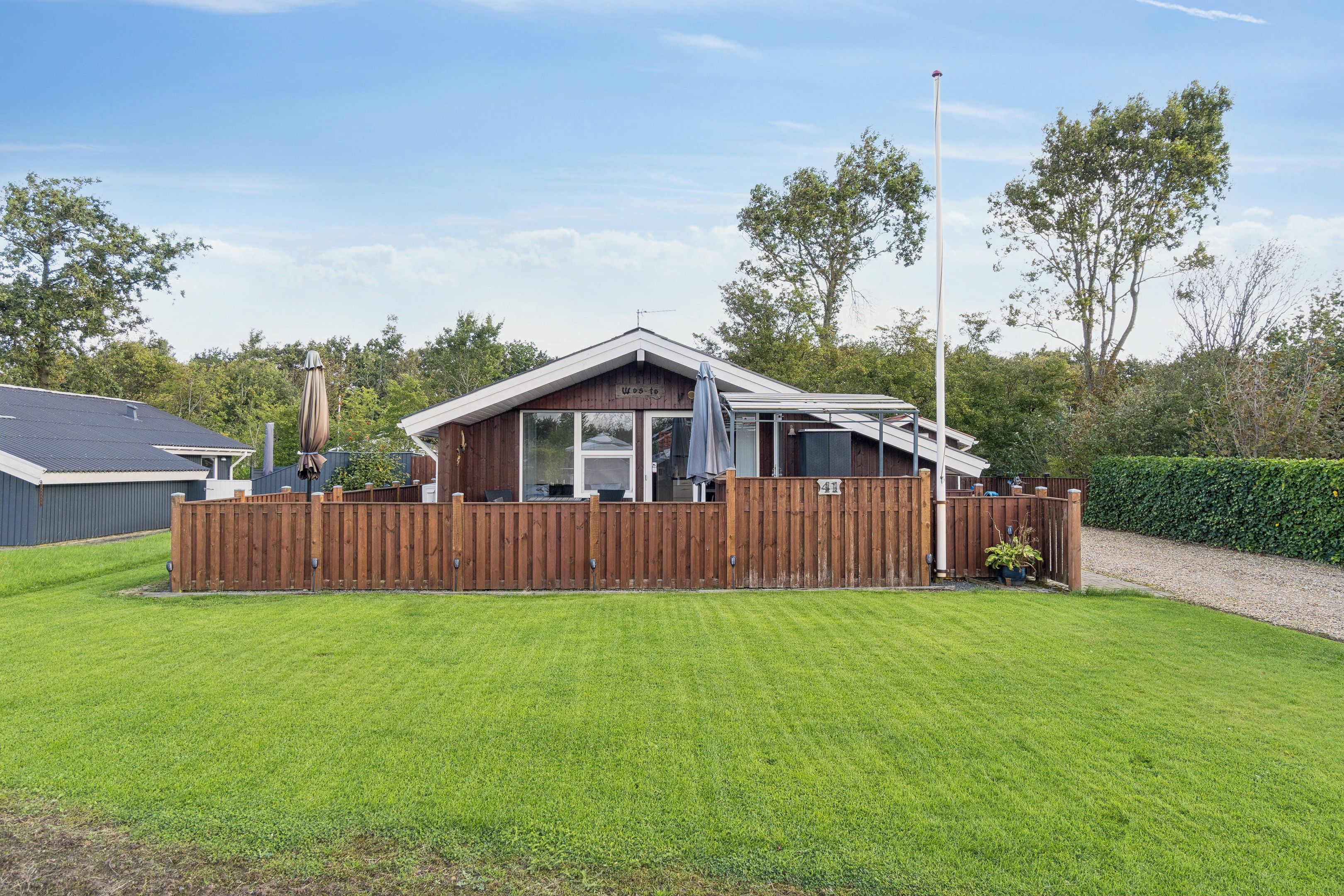 Une maison de plain-pied avec un jardin clôturé, un patio couvert et un mât pour drapeau.