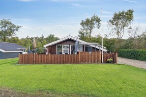 Ein eingeschossiges Haus mit einem umzäunten Garten, einer überdachten Terrasse und einer Fahnenstange.