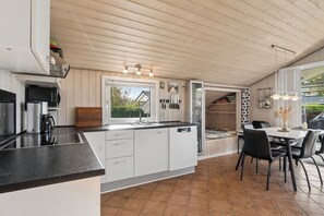 Eine moderne Küche mit einer zentralen Kochinsel, einem Essbereich mit Tisch und Stühlen und Blick durch das Fenster.