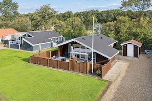 Ein Wohnhaus mit eingezäunter Terrasse, überdachter Sitzgelegenheit und einem kleinen Geräteschuppen.