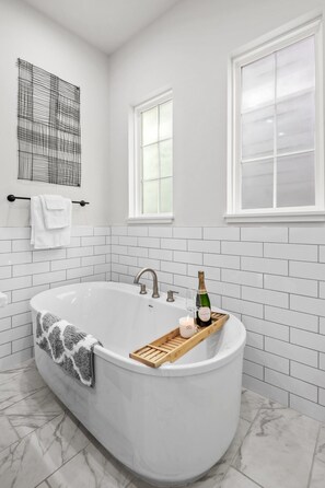 Ein modernes Badezimmer mit freistehender Badewanne, weißen Fliesenwänden und einem Marmorboden.