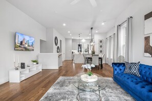 A modern living room with a blue sofa, a glass coffee table, and a cityscape painting on the wall.