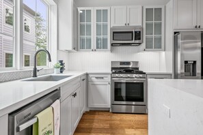 A modern kitchen with white cabinetry, stainless steel appliances, and a herringbone tile backsplash.