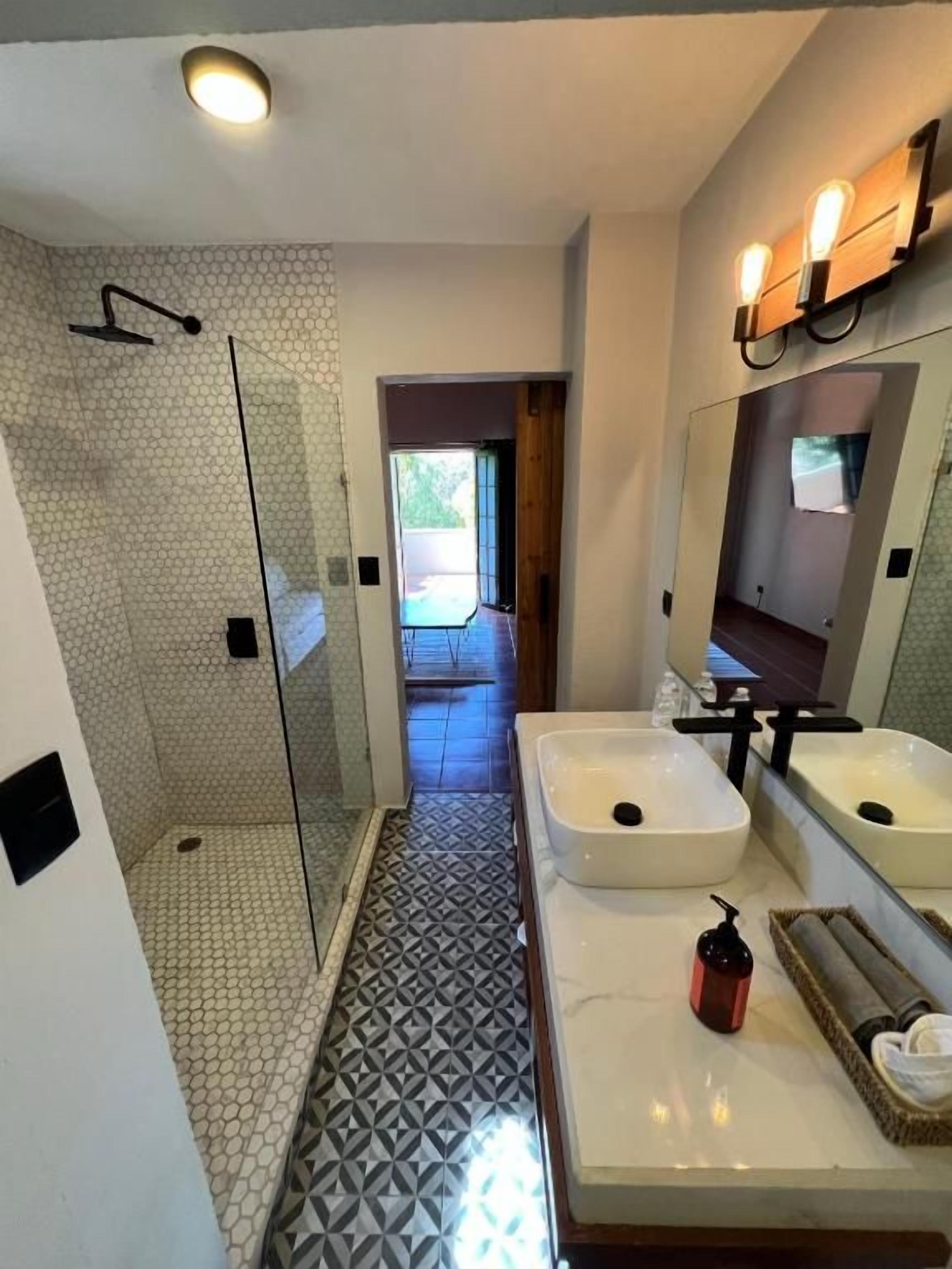 A modern bathroom with a glass-enclosed shower, two sinks, and a mirror with wall-mounted lights.