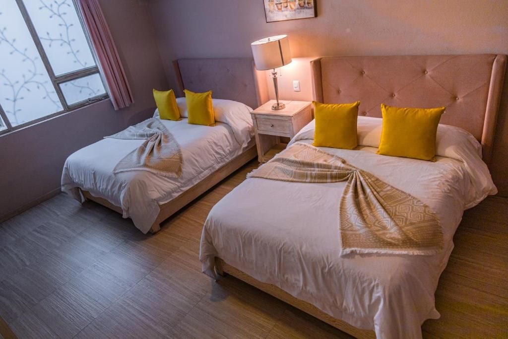 A hotel room with two beds, each with a headboard, a bedside table, and a lamp.
