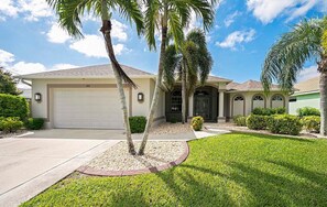 A single-story house with a garage, palm trees, and a well-maintained lawn. - Seva Retreat | Gulf Access | Pool |  Game Room (Cape Coral)