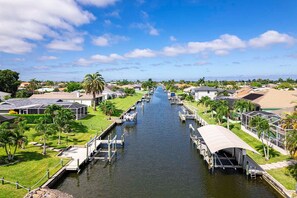 A canal with boats docked on both sides, surrounded by residential houses and greenery. - Seva Retreat | Gulf Access | Pool |  Game Room (Cape Coral)