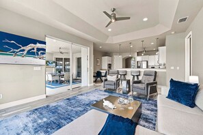 A modern living room with a sofa, coffee table, and chairs, a dining area with a table and chairs, and a kitchen with a refrigerator and cabinets. - Seva Retreat | Gulf Access | Pool |  Game Room (Cape Coral)