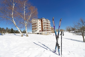 Schneebedeckte Landschaft mit einem mehrstöckigen Gebäude mit Balkonen und einem Paar Ski, die an einem Pfahl lehnen.