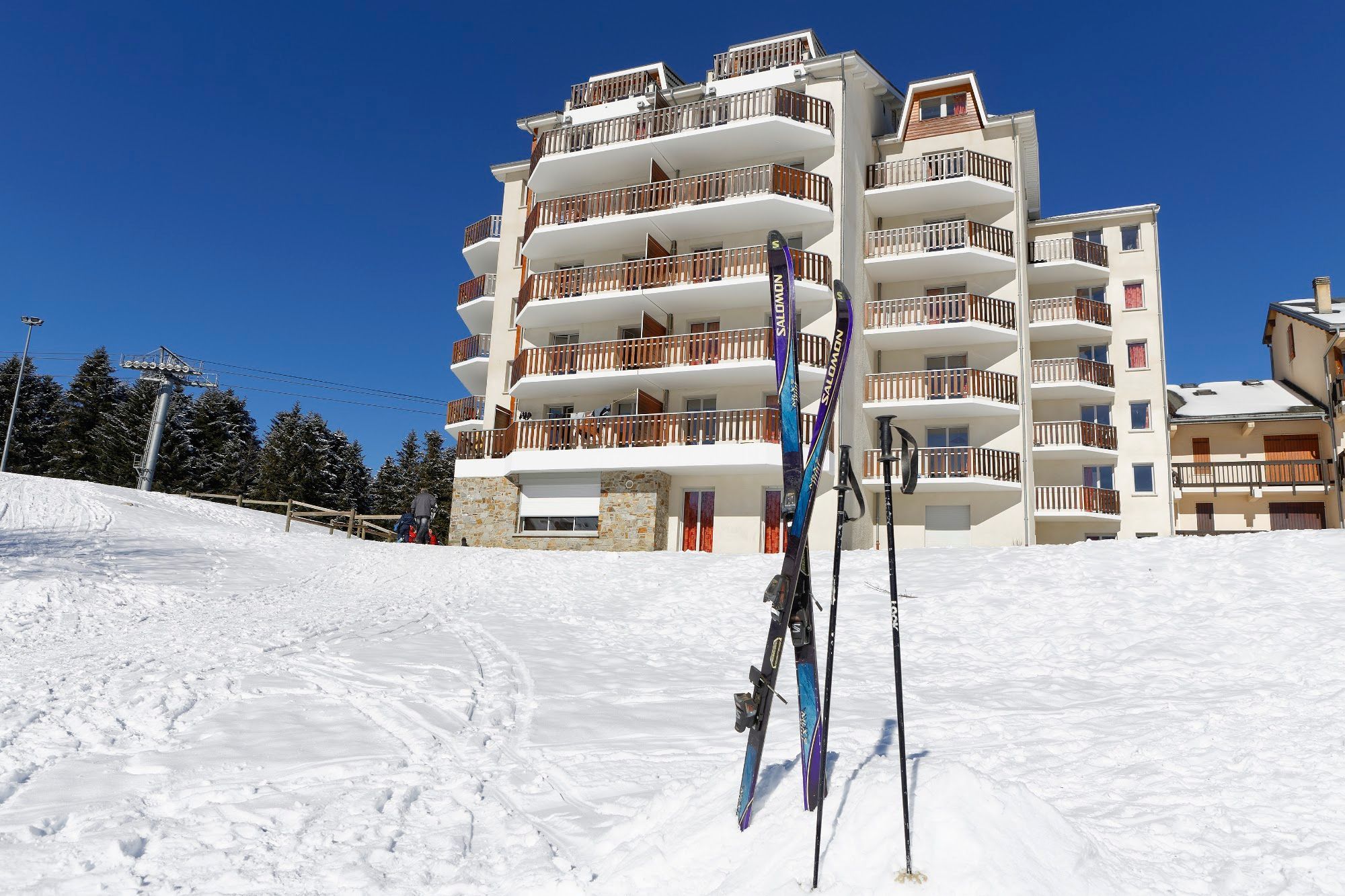 Een meerlaags gebouw met balkons, ski-uitrusting en een besneeuwde helling.
