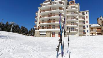 Een meerlaags gebouw met balkons, ski-uitrusting en een besneeuwde helling.