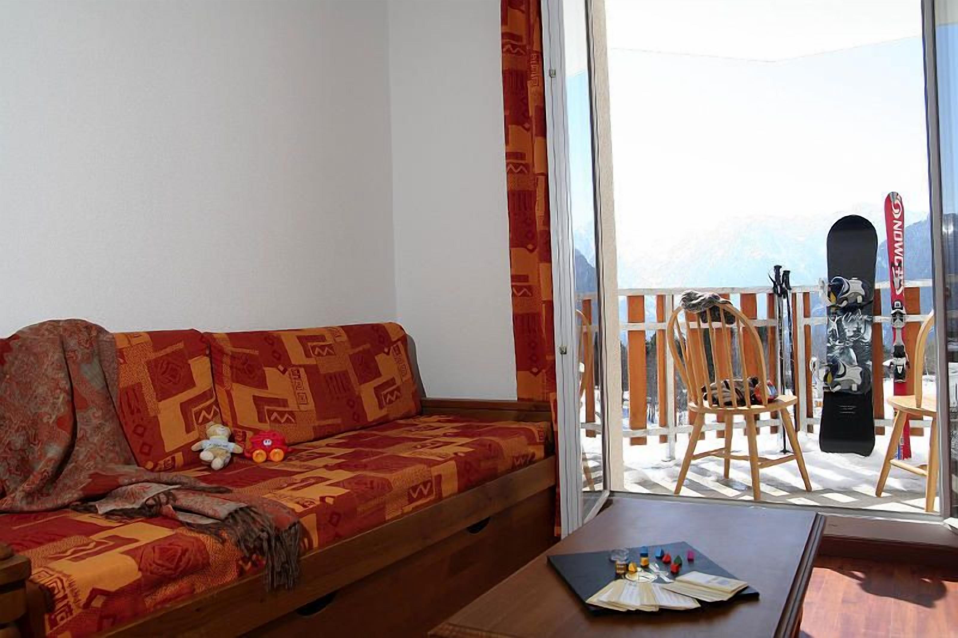 A room with a sofa, a table with a deck of cards, and a view of mountains through a balcony.