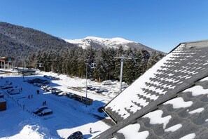 Un paysage montagneux enneigé avec un télésiège, un parking et un bâtiment doté d’un toit en pente.