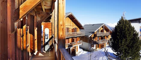 A wooden chalet with a balcony and a ski lift visible in the background.