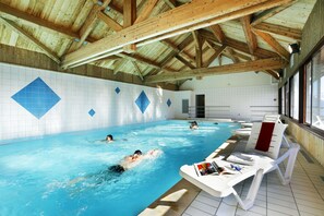 Piscina interna com vigas de madeira, paredes revestidas e espreguiçadeiras.