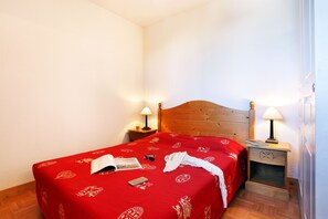 Une chambre d’hôtel avec une tête de lit en bois, un couvre-lit rouge à motifs, deux tables de chevet avec des lampes et un plancher en bois.