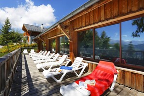A wooden deck with sun loungers and a red lounge chair, overlooking a mountainous landscape. - À deux pas des pistes & du centre | Accès piscine (La Toussuire)