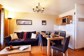 A compact living space with a sofa, dining table, chairs, a kitchen area, and a chandelier. - À deux pas des pistes & du centre | Accès piscine (La Toussuire)