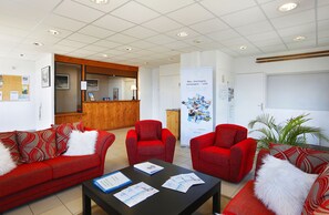 Un espace d’accueil avec un comptoir en bois, des chaises à revêtement rouge, une table noire où sont disposées des brochures et un panneau d’affichage où sont accrochées diverses annonces.