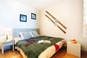 A bedroom with a bed, a nightstand, a lamp, a book, a pair of skis, and a basket of fruit. - À deux pas des pistes & du centre | Accès piscine (La Toussuire)