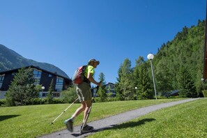 Eine Person wandert mit Rucksack auf einem Pfad, umgeben von Grünflächen und Gebäuden.