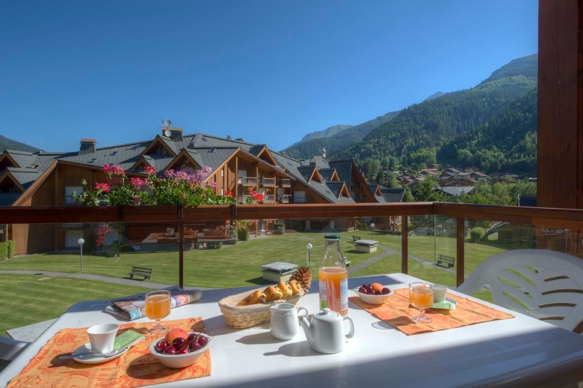 Une table de petit-déjeuner avec vue sur un village de montagne et un balcon doté de balustrades en bois.