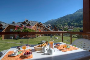 A breakfast table with a view of a mountain village and a balcony with wooden railings. - Bain à remous sur place |  Commerces à 200m (Les Contamines-Montjoie)