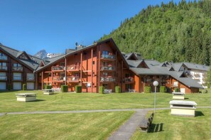 A multi-story lodge with balconies, a well-maintained lawn, and a mountainous backdrop. - Bain à remous sur place |  Commerces à 200m (Les Contamines-Montjoie)