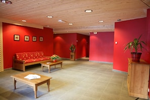 Un hall aux murs rouges, avec un canapé en bois, une table en bois et une plante en pot.