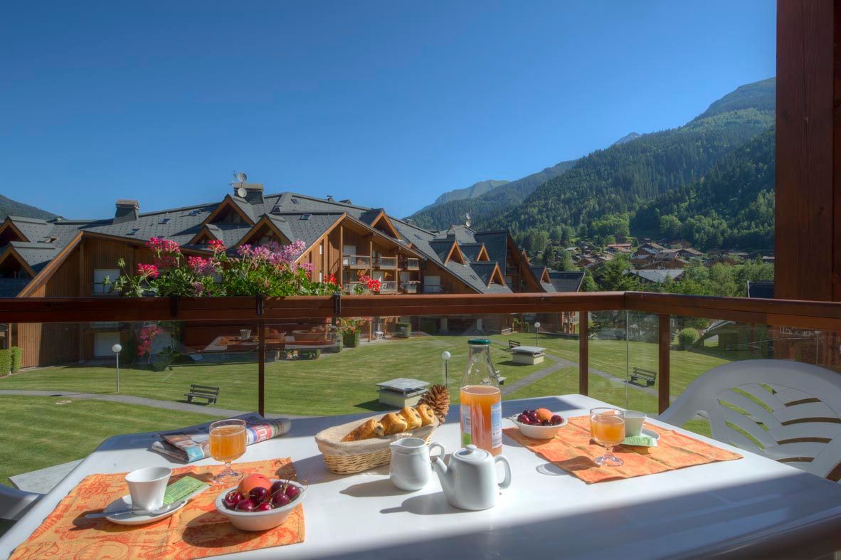 Une table de petit-déjeuner avec vue sur un village de montagne et un balcon doté de balustrades en bois.