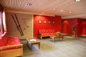 Une pièce avec un canapé rouge, un banc en bois, une petite table et un mur orné de tableaux.