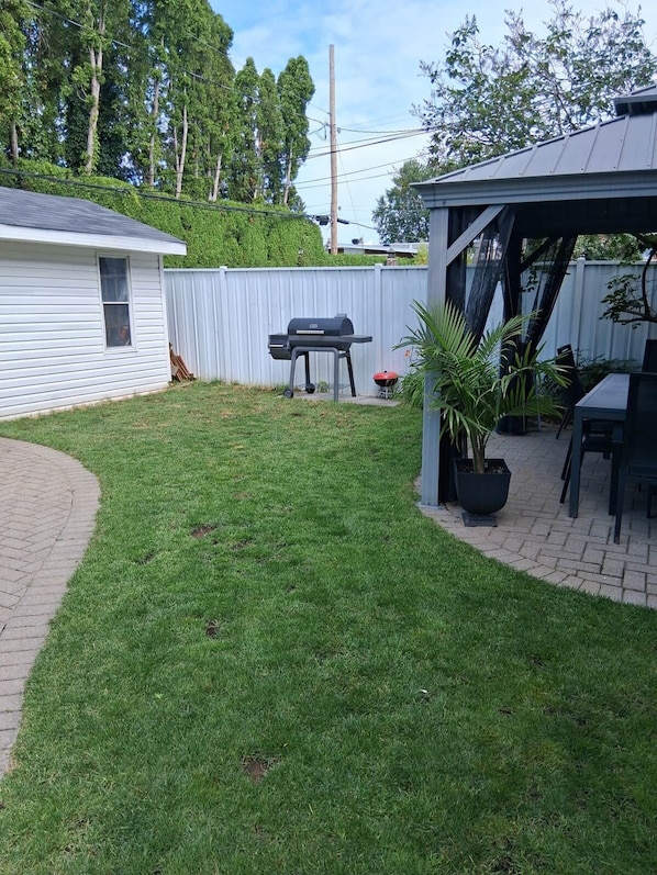 A backyard with a barbecue grill, a covered patio area, and a fenced yard. - Cozy, Beautifull and very peacefull apartment. (Longueuil)