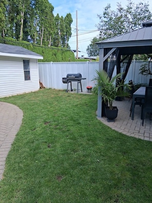 Een achtertuin met een barbecue, een overdekte patio en een omheind gazon.