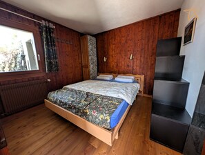 A bedroom with a wooden bed, a window with curtains, a radiator, and a black cabinet. - Apartment with large terrace and stunning views of the MatterhornOutside: apartment located on the g (St-Luc)