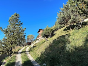 A mountain lodge with a dirt path leading to it, surrounded by trees and a clear blue sky. - Apartment with large terrace and stunning views of the MatterhornOutside: apartment located on the g (St-Luc)
