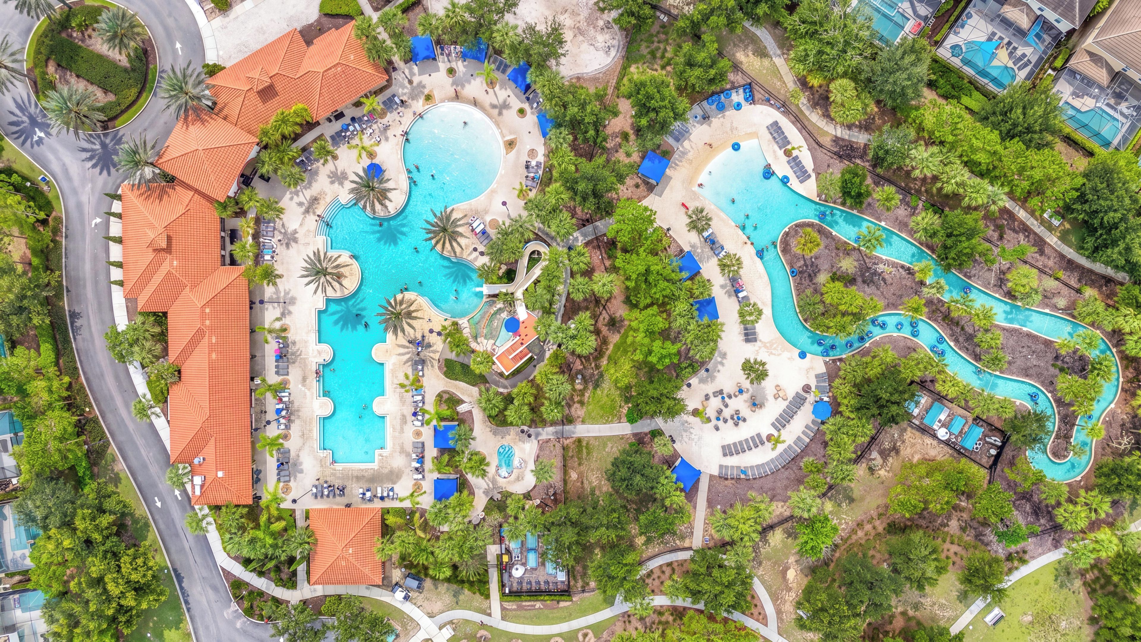 Luchtbeeld van een resort met meerdere zwembaden, palmbomen en een kronkelende waterglijbaan.