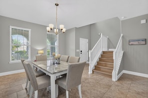 A dining area with a marble table, four chairs, a chandelier, and a view of the outdoors through large windows with blinds. - Spacious 5-bedroom house in lovely Davenport with AC (Davenport)