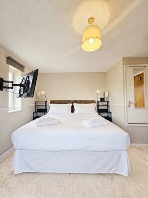 Une chambre d’hôtel avec un grand lit, un téléviseur à écran plat fixé au mur, des lampes de chevet et une porte dotée d’un panneau en bois.