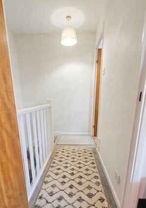 A hallway with a patterned carpet, white walls, a ceiling light, and a door at the end.