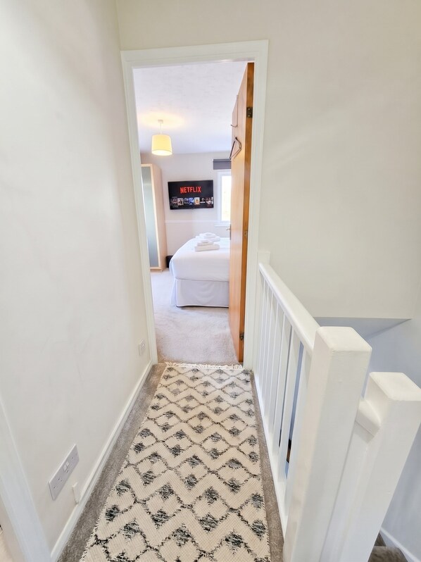A hallway leading to a bedroom with a white bed and a television displaying the Netflix logo.
