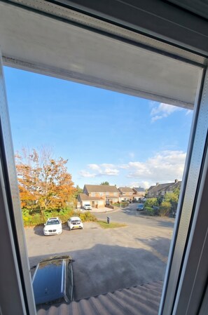 A view through a window of a residential area with houses, parked cars, and a clear sky.