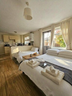 Een hotelkamer met een tweepersoonsbed, een klein kitchenette, een eethoek en een groot raam met gordijnen.