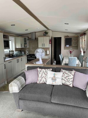A compact living space with a kitchenette, a sofa with decorative pillows, and a fan. - Charming Tattershall Mobile Home 3 Bedrooms, Private Entrance, Shared Pool (Lincoln)