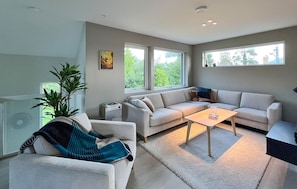 A modern living room with a sofa, a coffee table, and a large window providing a view of greenery outside. - Lovely home in Kolbjørnsvik with sauna (Kolbjørnsvik)