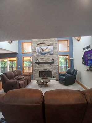 A living room with a stone fireplace, leather sofas, and a mounted television.