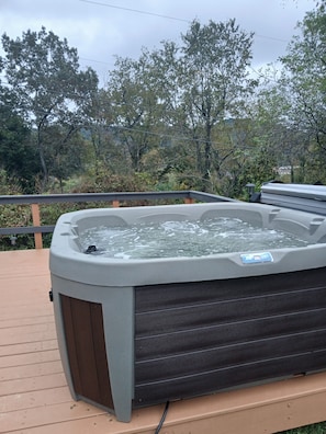 A hot tub on an outdoor deck with a wooden railing and trees in the background.